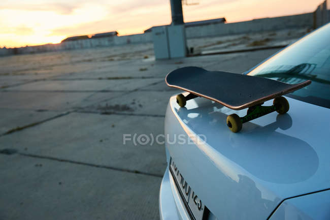 Skateboard on car trunk at sunset — Stock Photo