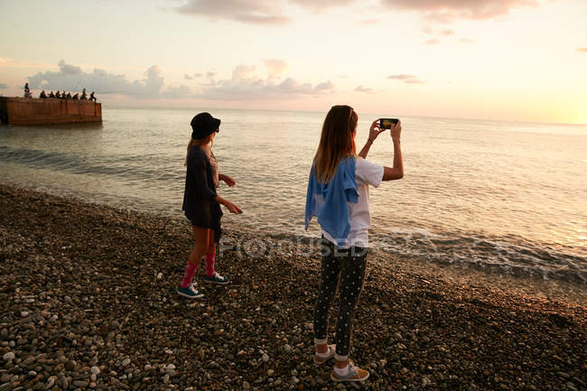 Chica tomando fotos del mar con su amigo - foto de stock