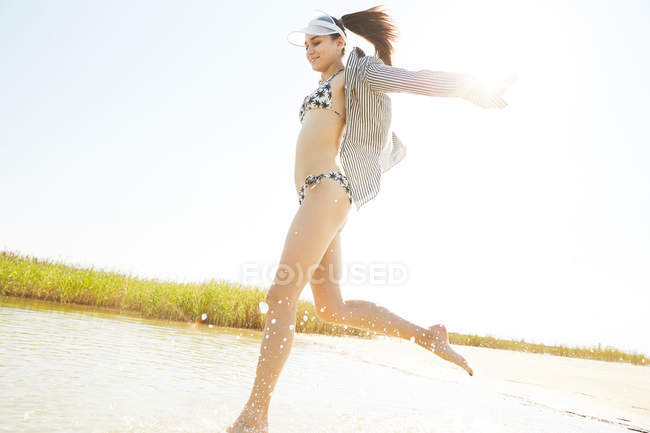 Mujer en visera blanca corriendo en la playa - foto de stock