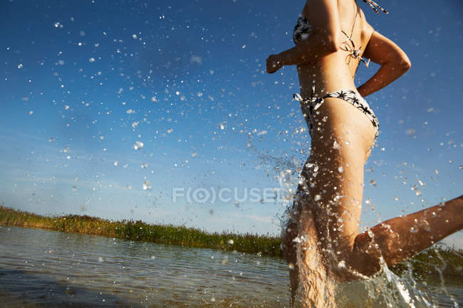 Woman in swimsuit running in water — Stock Photo