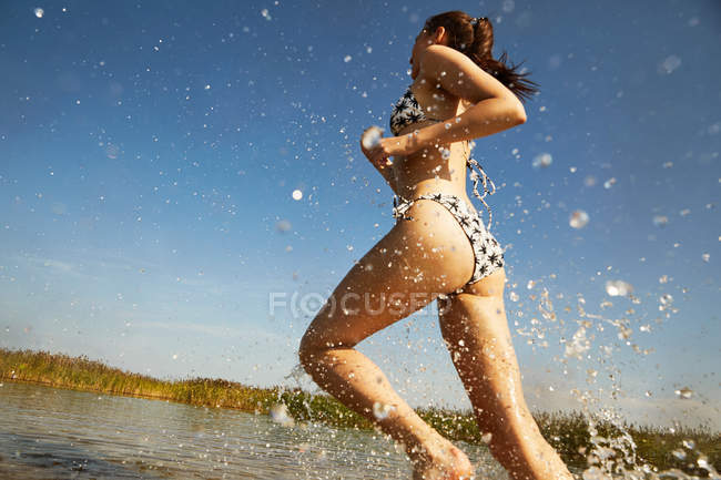Donna in costume da bagno in esecuzione in spruzzi d'acqua — Foto stock