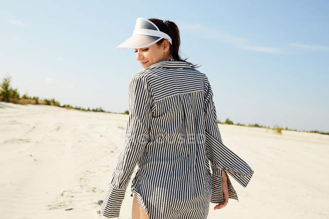 Femme en visière marchant sur la plage — Photo de stock