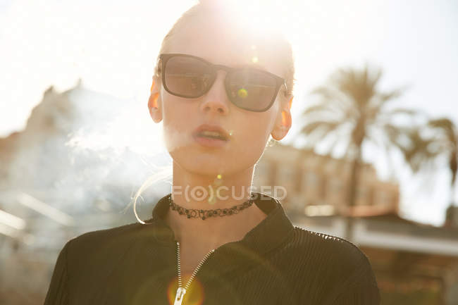 Retrato de jovem mulher em óculos de sol fumando cigarro eletrônico na rua em barcelona — Fotografia de Stock