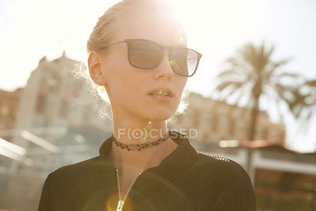 Portrait of beautiful woman in sunglasses standing on street at sunny day — Stock Photo