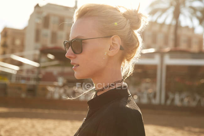Side view of attractive girl in sunglasses standing on street at sunny day — Stock Photo