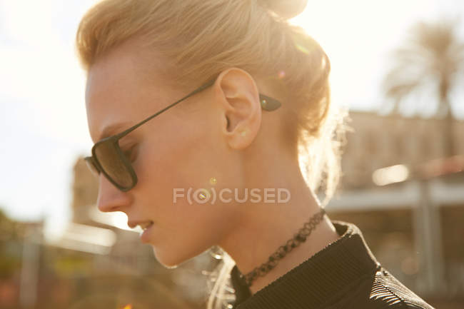 Side view of attractive woman in sunglasses standing on street at sunny day — Stock Photo