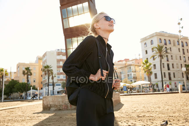 Bela mulher em óculos de sol e saco andando na praia pública em barcelona — Fotografia de Stock