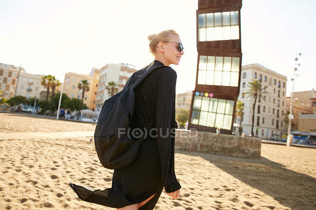 Cheerful attractive woman in sunglasses and bag walking on public beach in barcelona — Stock Photo