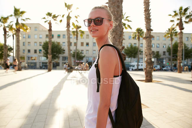 Blonde young tourist with black bag and sunglasses standing on street in barcelona — Stock Photo