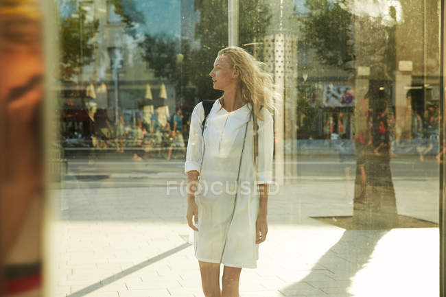Jovem mulher de pé perto de vidro na rua em barcelona e olhando para longe — Fotografia de Stock