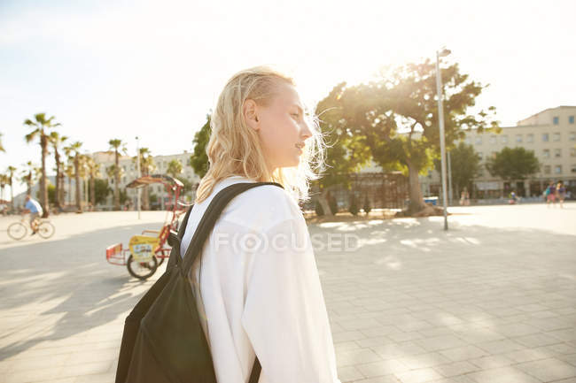 Vista lateral de mujer joven caminando con bolso en la calle en barcelona - foto de stock