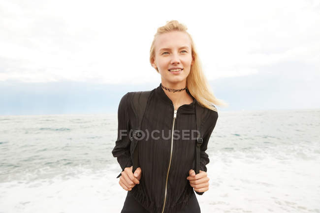 Portrait of beautiful woman in black dress and bag standing near sea — Stock Photo