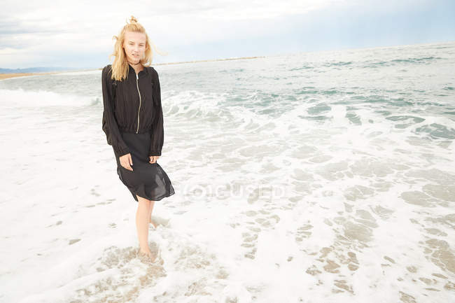 Bella donna in abito nero e borsa in piedi in mare — Foto stock