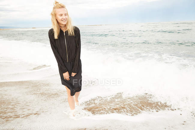 Felice bella donna in abito nero e borsa in piedi in mare — Foto stock