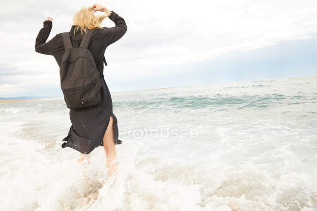 Vue arrière de la femme en robe noire et sac s'amuser en mer — Photo de stock