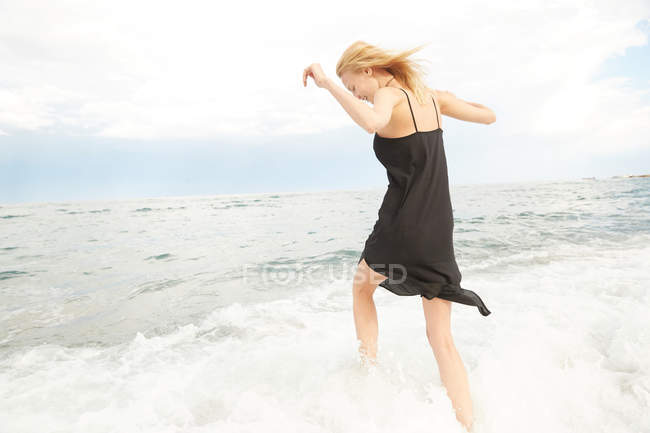 Belle femme en robe noire s'amuser en mer — Photo de stock