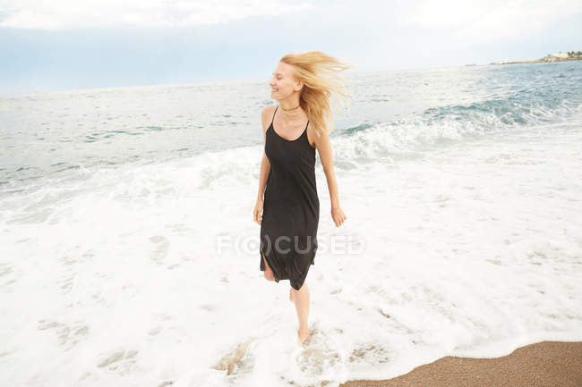 Счастливая красивая женщина в черном платье прогуливается по морскому пляжу — стоковое фото