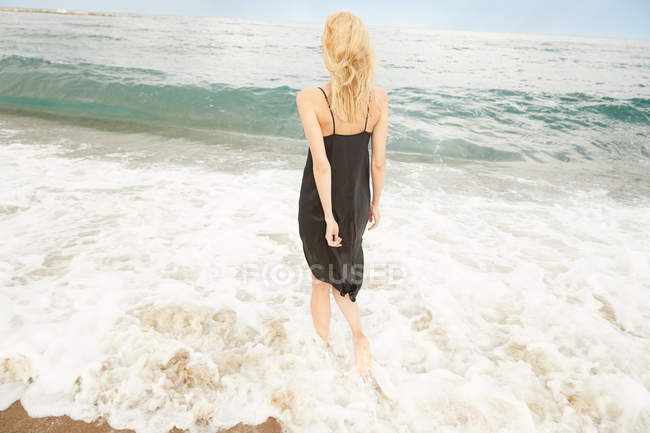 Задний вид женщины в черном платье, стоящей в море — стоковое фото