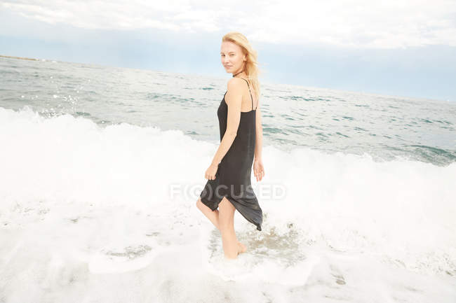 Beautiful woman in black dress standing in sea — Stock Photo