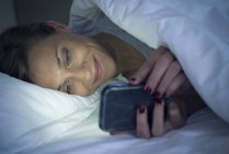 Жінка лежить в ліжку за допомогою смартфона — стокове фото