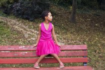 Mädchen sitzt allein auf Parkbank und schaut gedankenverloren weg — Stockfoto