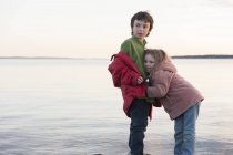 Little girl hugging her brother at water's edge — Stock Photo