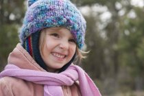 Маленькая девочка в вязаной шляпе и шарфе, улыбающаяся, портрет — стоковое фото