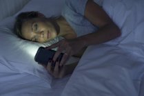 Femme couchée au lit en utilisant un smartphone — Photo de stock