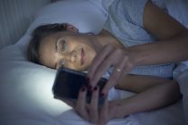 Mulher na cama usando smartphone — Fotografia de Stock