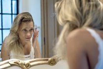 Woman looking bleary-eyed at self in bathroom mirror — Stock Photo