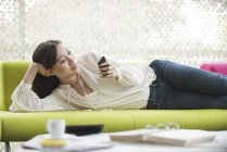 Жінка розслабляється вдома за допомогою смартфона — стокове фото