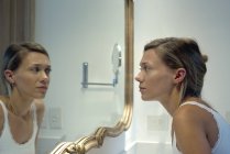 Женщина смотрит на себя в зеркало ванной — стоковое фото