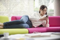 Жінка розслабляється вдома зі смартфоном — стокове фото