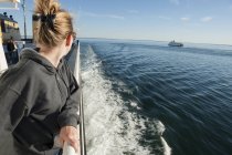 Woman standing on deck of ferry boat, looking over shoulder at view — Stock Photo