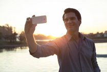 Hombre usando smartphone para fotografiarse delante del atardecer - foto de stock