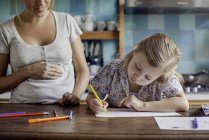Schwangere Mutter sieht zu, wie Tochter mit Filzspitzen zeichnet — Stockfoto