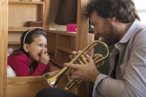 Отец играет на трубе для маленькой девочки, лежащей в постели — стоковое фото