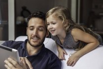 Мужчина показывает дочери видео потоковое на цифровом планшете — стоковое фото