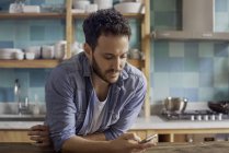 Man at home in kitchen text messaging — Stock Photo