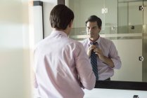 Чоловік дивиться у дзеркало у ванній кімнаті, регулюючи краватку — стокове фото