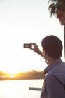 Чоловік фотографує захід сонця зі смартфоном — стокове фото