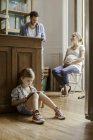 Ragazza seduta da sola a giocare al videogioco mentre i genitori chattano — Foto stock