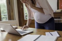 Femme enceinte utilisant un ordinateur portable et passer un appel téléphonique — Photo de stock