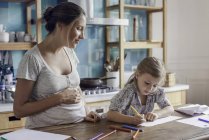 Mãe grávida assistindo filha desenho com canetas de feltro na cozinha — Fotografia de Stock