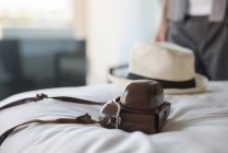 Câmera e chapéu de palha na cama no quarto do hotel — Fotografia de Stock
