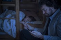 Pai verificando smartphone enquanto conforta a filha doente — Fotografia de Stock