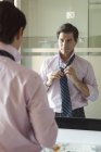 Чоловік регулює краватку у дзеркалі ванної кімнати — стокове фото