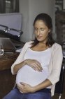 Retrato da mulher grávida embalando barriga sentada na cadeira em casa — Fotografia de Stock