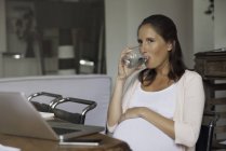 Беременная женщина пьет воду из стекла — стоковое фото
