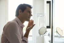 Hombre mirando en el espejo y la aplicación de moisurizer a la cara - foto de stock